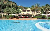 Großer Außenpool vor einem mediterranen Hotelgebäude mit Sonnenterrasse, Palmen und grüner Hügellandschaft im Hintergrund – sonnige Urlaubsatmosphäre unter blauem Himmel.