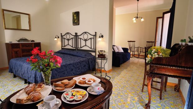 Gemütliches Doppelzimmer mit traditionellem Mobiliar, gemustertem Fliesenboden und separatem Sitzbereich – auf dem Tisch ein liebevoll angerichtetes Frühstückstablett mit Kaffee, Gebäck und frischen Blumen.