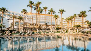 Großzügiger Poolbereich mit Liegen unter Palmen – ideal zum Entspannen und Genießen der Sonne direkt vor dem eleganten Hotelgebäude.