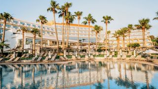Großzügiger Poolbereich mit Liegen unter Palmen – ideal zum Entspannen und Genießen der Sonne direkt vor dem eleganten Hotelgebäude.