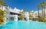 Weitläufige Poollandschaft eines weißen Luxusresorts mit Palmen, Wasserfällen und türkisblauem Wasser – perfekte Kulisse für einen entspannten Urlaub in der Sonne.