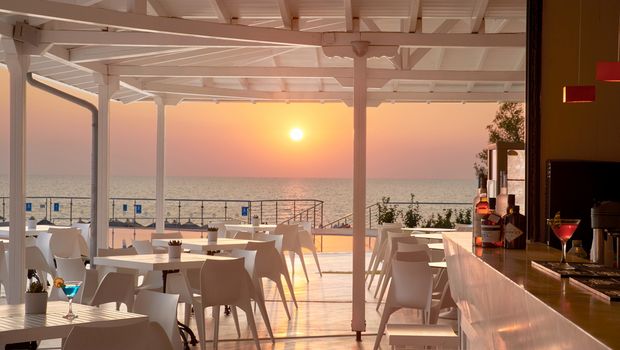 Stilvolle Hotelbar mit weißem Interieur und traumhaftem Blick auf das Meer – ideal, um den Sonnenuntergang bei einem Cocktail in entspannter Atmosphäre zu genießen.