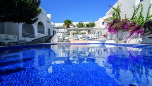 Großer Außenpool eines mediterranen Hotels mit Sonnenliegen, weißen Gebäuden, Palmen und blühender Bougainvillea – perfekte Kulisse für entspannte Urlaubsmomente.
