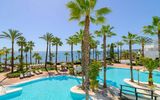 Großzügige Poollandschaft mit Palmen und Meerblick in einer tropischen Hotelanlage bei strahlend blauem Himmel.