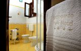 Helles Badezimmer mit gelb gefliesten Wänden und Dusche, im Vordergrund ein besticktes Handtuch mit dem Schriftzug „Gattopardo Park Hotel“ und vier Sternen.