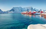 Rote Häuser am Ufer des Norwegischen Meeres. Sonnige Winteransicht des Fischerdorfes Sakrisoy