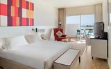 Modern eingerichtetes Hotelzimmer mit großem Doppelbett, stilvollem Sessel, Flachbild-TV und Zugang zu einem möblierten Balkon mit Meerblick.
